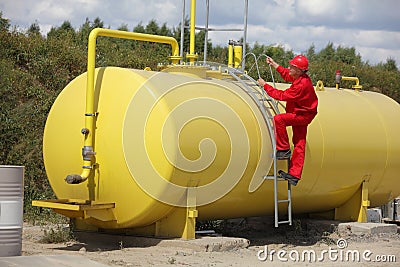 Technician in uniform climbing on large fuel tank Stock Photo