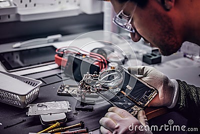 Technician uses a magnifying glass to carefully inspect the internal parts of the smartphone in a modern repair shop Stock Photo