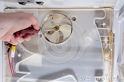 A technician uses a screwdriver in refrigerator fridge. Inside refrigerator repair. Disassembled refrigerator. Removed Stock Photo