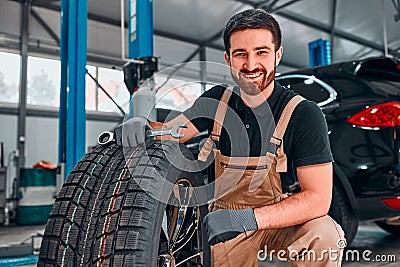 A technician in workwear, holding a wrench and a car tire in tire fitting Stock Photo