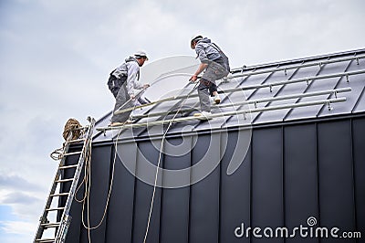 Technicians carrying photovoltaic solar module while installing solar panel system on roof of house Stock Photo