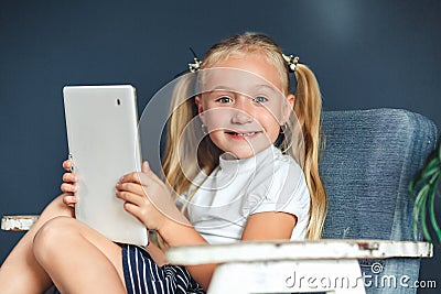 Technologies, people concept - young blondy girl sitting on a chair and watching the tablet or surfing the net, looking at camera Stock Photo