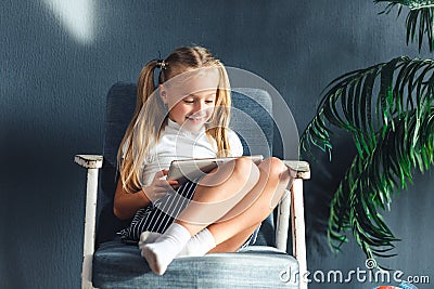 Technologies, people concept - young blondy girl sitting on a chair and watching the tablet or surfing the net and smiling Stock Photo