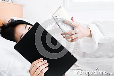 Asian Woman Engrossed in Mobile Phone and Tablet Usage, Exploring Nomophobia Concept Stock Photo