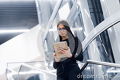 Technology, business and corporate concept - happy woman or student with tablet pc computer standing on stairs at modern Stock Photo