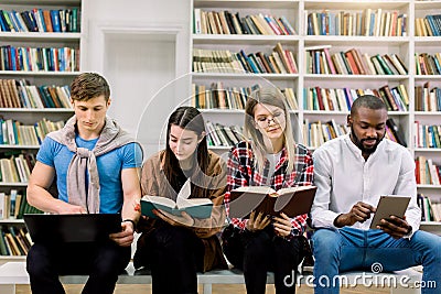 Technology, computers, ebooks and traditional print books in education. Team of multiethnic students, two boys and two Stock Photo