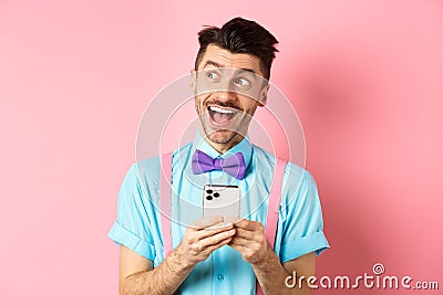 Technology concept. Excited man looking aside with dreamy face, winning online prize on smartphone, standing cheerful Stock Photo