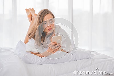 Technology, free time, communication concept. Cheerful white skinned teenager with blonde hair, dressed in nightwear, uses mobile Stock Photo