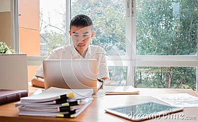 Technology Learning concept: Asian Young man student learning and check timetable for projected in laptop computer at busy table Stock Photo