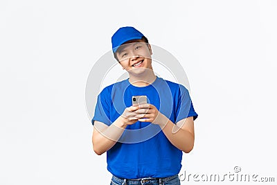 Technology, online shopping and shipping concept. Cheerful smiling asian courier in blue uniform, tracking shipment Stock Photo