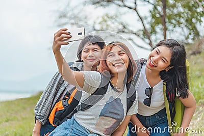 Technology, travel, tourism, jungle hike and people concept - group of smiling friends with backpacks taking selfie by smartphone Stock Photo