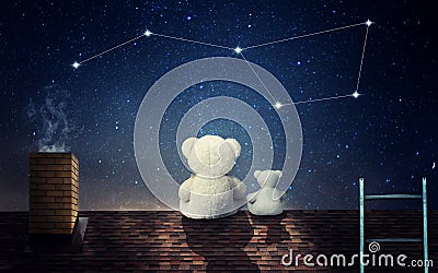 A teddy bear with a little bear sits at night on the roof of the house and looks at the constellation of the big bear. Stock Photo