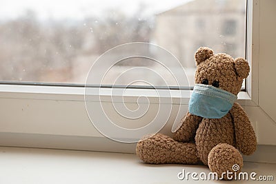 Teddy bear in a medical mask on the window in the apartment, children`s morbidity during Stock Photo