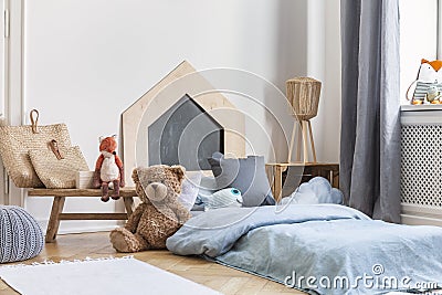 Teddy bear next to a bed covered with blue sheets in a natural kid room interior. Real photo Stock Photo