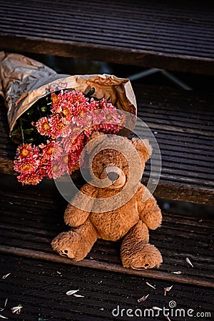 A teddy brown bear sits on wooden steps next to chrysanthemums. Stock Photo