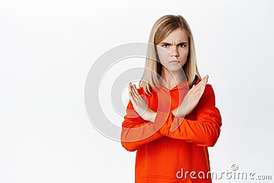 Teen blond girl showing cross, stop rejection gesture, prohibit smth, disagree, showing taboo block, standing over white Stock Photo