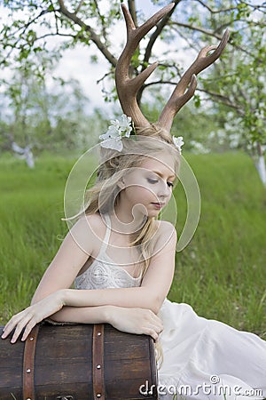 Teen blonde girl wearing white dress with deer horns on her head Stock Photo