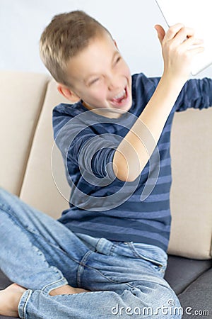 Child sitting on couch and using tablet computer. Teen boy annoyed and frustrated shouting with anger while playing computer games Stock Photo