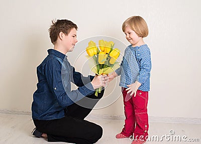 Teen boy congratulates his little sister and gives her flowers tulips Stock Photo