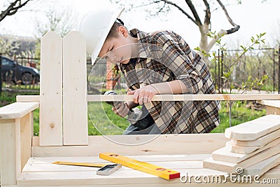 Teen boy in helmet with a screwdriver making a garden bench outdoors. Stock Photo