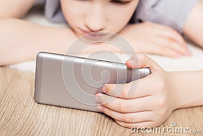 Teen boy lies on carpet and watches video in smartphone. Selective focus on smartphone Stock Photo
