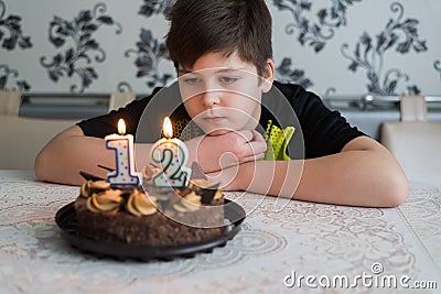 Teen boy looks thoughtfully at cake with candles on twelfth day of birth Stock Photo