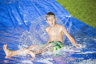 Teen boy sliding down a slip and slide outdoors Stock Photo