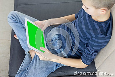 Teen boy using tablet pc with green screen while sitting on sofa at home. Close up of thumb scrolling up through touch screen Stock Photo