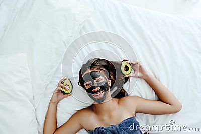 Teen girl applying black clay facial mask with avocado Stock Photo