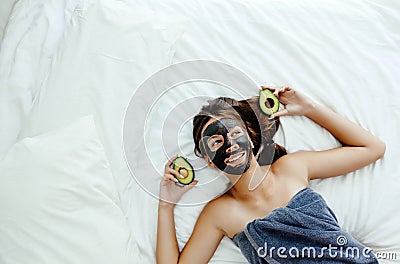 Teen girl applying black clay facial mask with avocado Stock Photo