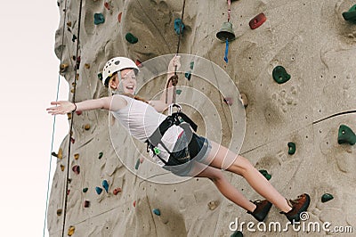 A teen girl climbing on a rock wall leaning back against the rope. Stock Photo