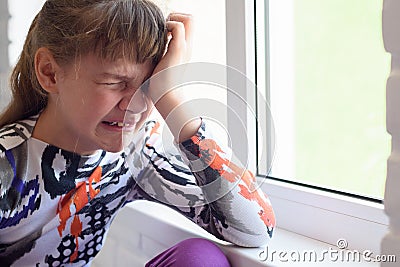 Teen girl crying a lot while sitting by the window in the room, close-up Stock Photo