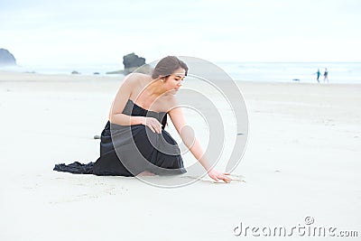 Teen girl in dress kneeling, writing in sand on beach Stock Photo