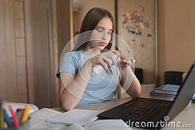 Teen girl, home lessons laptop, antiseptic spray, disinfection of hands from bacteria and viruses, video tutoring Stock Photo