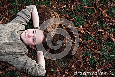 Teen girl laying on autumn ground with long hair scattered on grass. Stock Photo