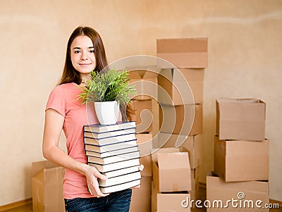 Teen girl moving house to college, holding pile books and plant Stock Photo