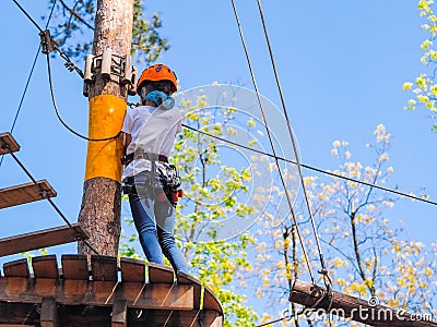 Teen girl in orange helmet climbing in trees in forest adventure park Stock Photo