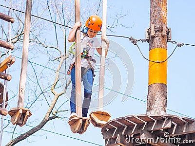 Teen girl in orange helmet climbing in trees in forest adventure park Stock Photo