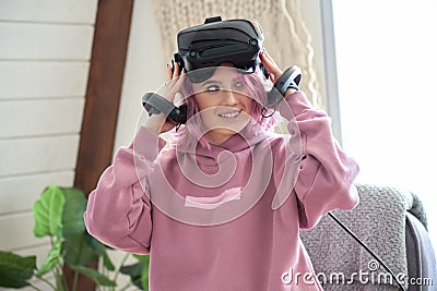 Teen girl pink hair wear vr headset hold controllers experience virtual reality. Stock Photo