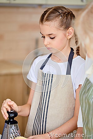 teen girl preparing food in kitchen, using grater, looking down Stock Photo