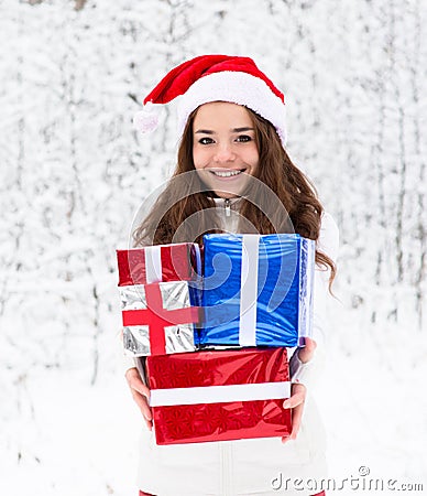 Teen girl with santa hat and red gift boxes standing in winter forest Stock Photo