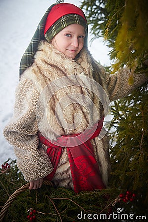 Teen girl in thick coat and a red sash with basket of fir branches and berries in cold winter day in forest. Medieval Stock Photo