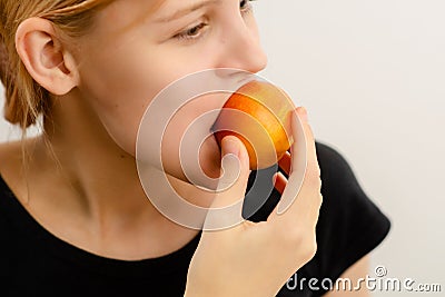 Teen's healthy snacking: A young woman with a slender build bites into a ripe yellow plum, experiencing the health Stock Photo