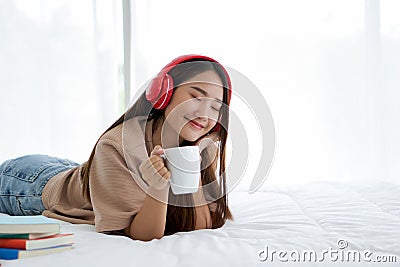 Teen wearing headphones drinking a cup of coffee relax on bed at home after reviewing the textbook Stock Photo