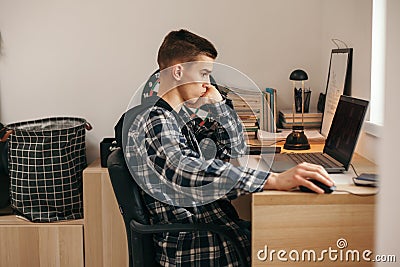 Teenage boy doing homework using computer sitting by desk in room alone Stock Photo