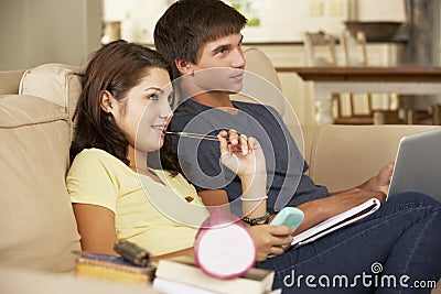 Teenage Boy And Girl Sitting On Sofa At Home Doing Homework Using Laptop Computer Whilst Holding Mobile Phone Stock Photo