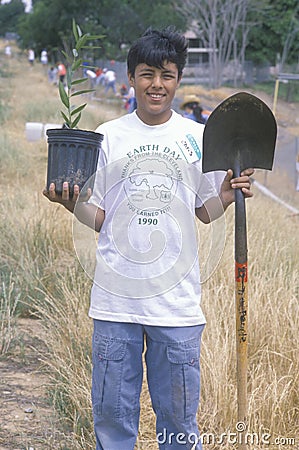 A teenage boy holding a plant and a shovel during Earth Day participation Editorial Stock Photo