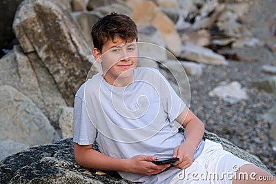 teenage boy lies on the beach phone in hand on the Stone Shore lie on the Big Stone sunny day ocean rest relaxation Stock Photo