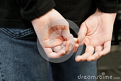 The teenage boy is nervous and embarrassed, holding his hands behind his back with crossed fingers. Emotional stress. Close-up. Stock Photo