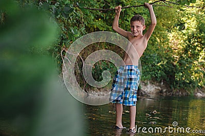 A teenage boy in shorts plays in a mountain river in shallow water Stock Photo